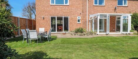 A two-story brick house with a patio, a conservatory, and a fenced backyard.