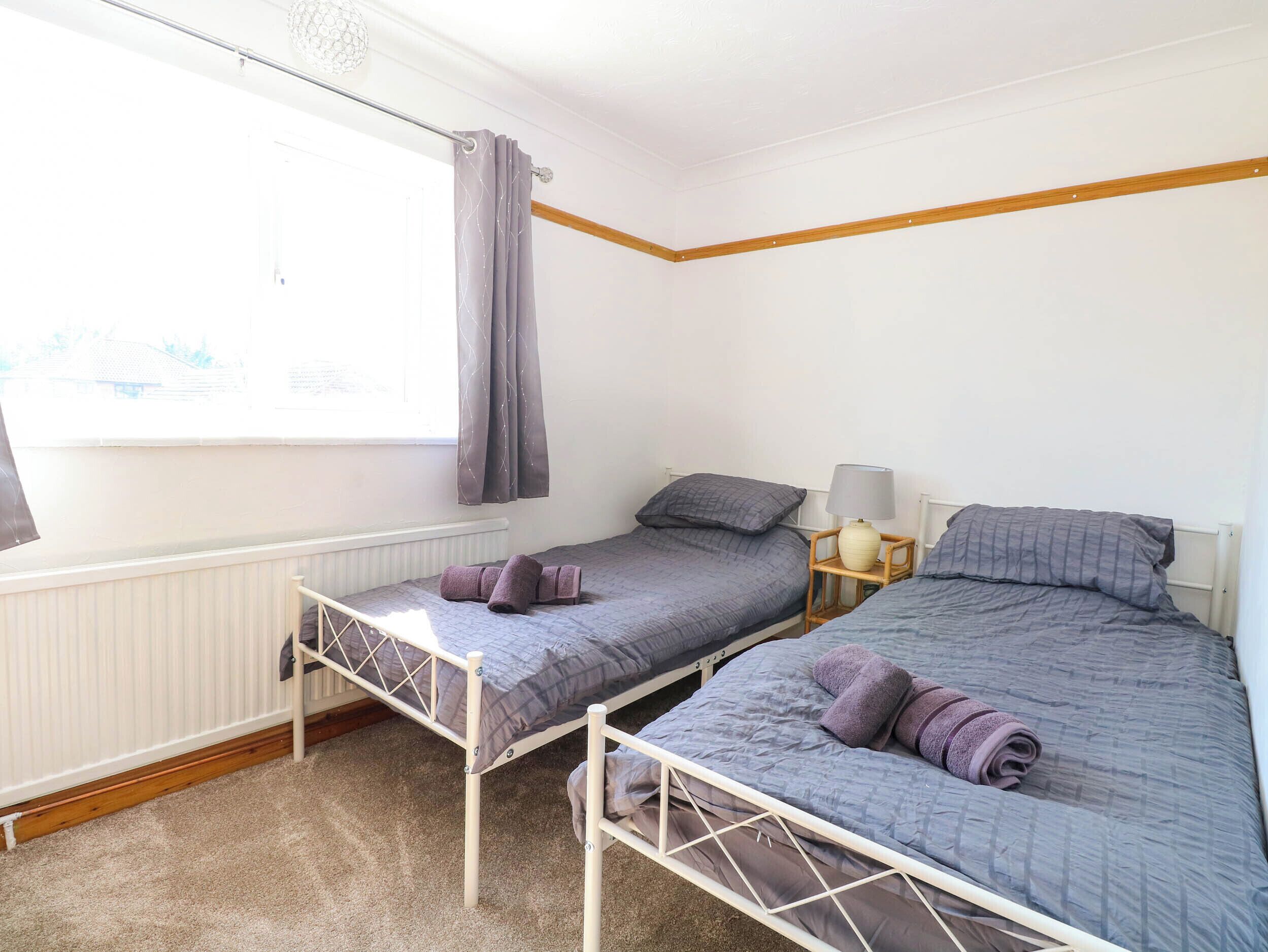 Ein Schlafzimmer mit zwei Einzelbetten, einem Fenster mit Vorhängen, einem Nachttisch mit Lampe und einem Heizkörper.