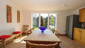 A spacious dining area with a wooden table and chairs, a blue bowl centerpiece, and a view of the garden through large windows. - Cedar View (Norwich)