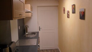 Un couloir étroit, avec une kitchenette sur la gauche, une porte blanche sur la droite et un petit évier.