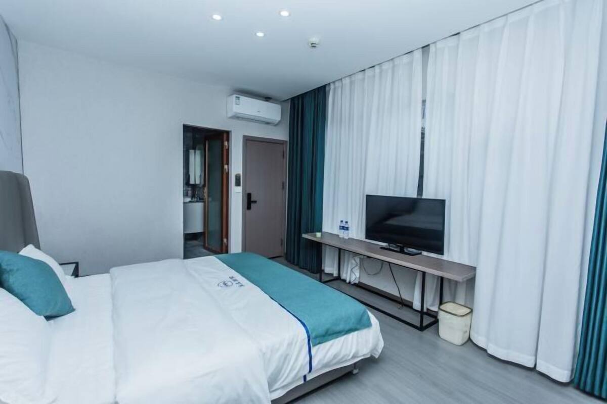 A hotel room with a bed, a TV, a desk, and a window with curtains.