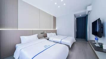 A hotel room with two beds, a flat-screen TV, a desk, and a bathroom visible through a door.