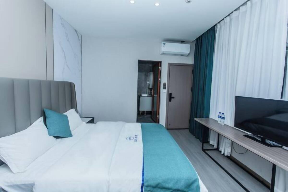 A hotel room with a bed, a TV, a desk, and an air conditioning unit.