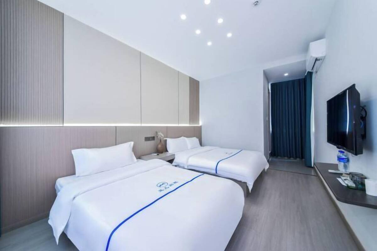 A hotel room with two beds, a TV, a desk, and a bathroom visible through an open door.