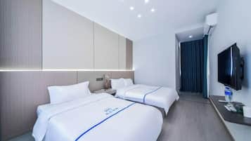A hotel room with two beds, a TV, a desk, and a bathroom visible through an open door.