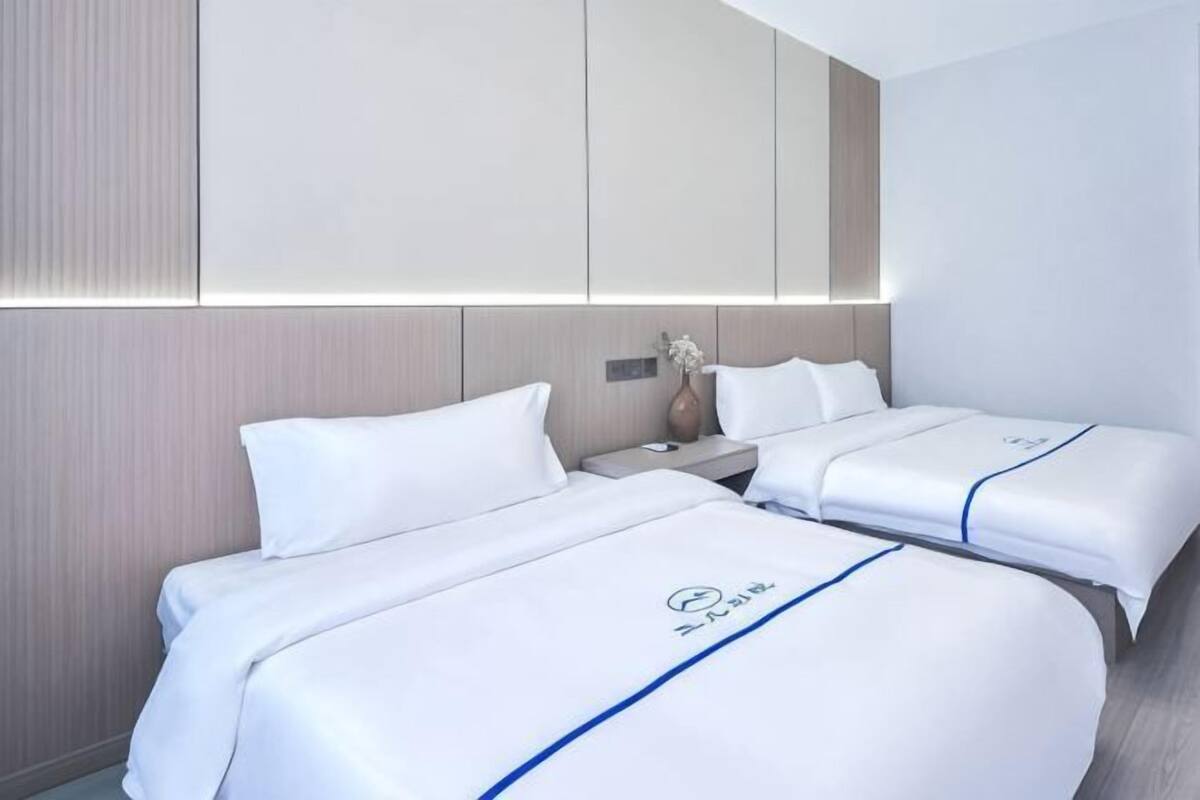 A hotel room with two beds, a nightstand, a vase with flowers, and a large mirror above the beds.