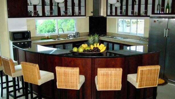 Una cocina con una isla central, taburetes de bar y un refrigerador.