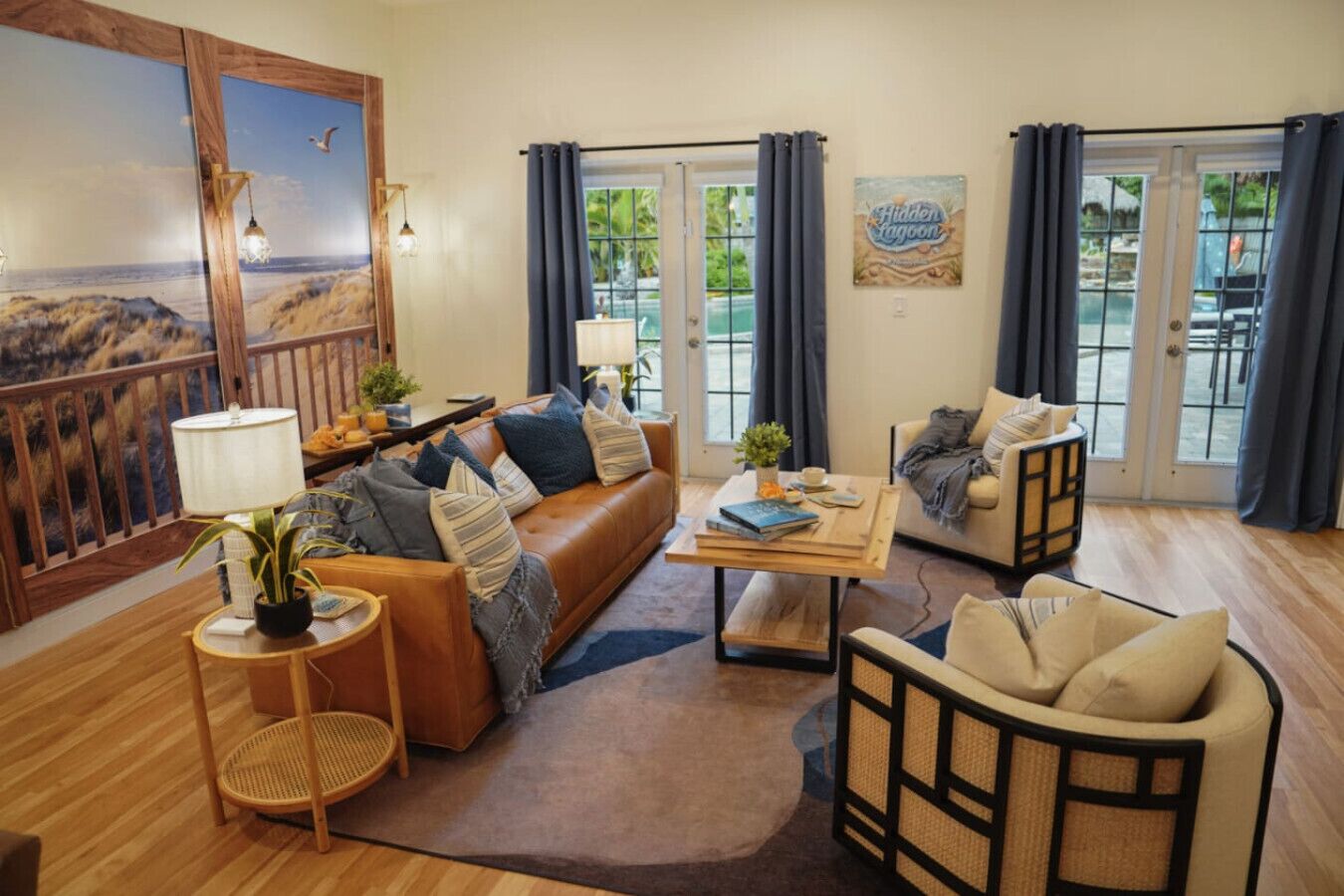 Un salon chaleureux avec un canapé en cuir, une table basse en bois et deux fauteuils. Un grand tableau orne le mur, une plante en pot est posée à proximité, et on peut admirer le paysage extérieur à travers les portes vitrées.