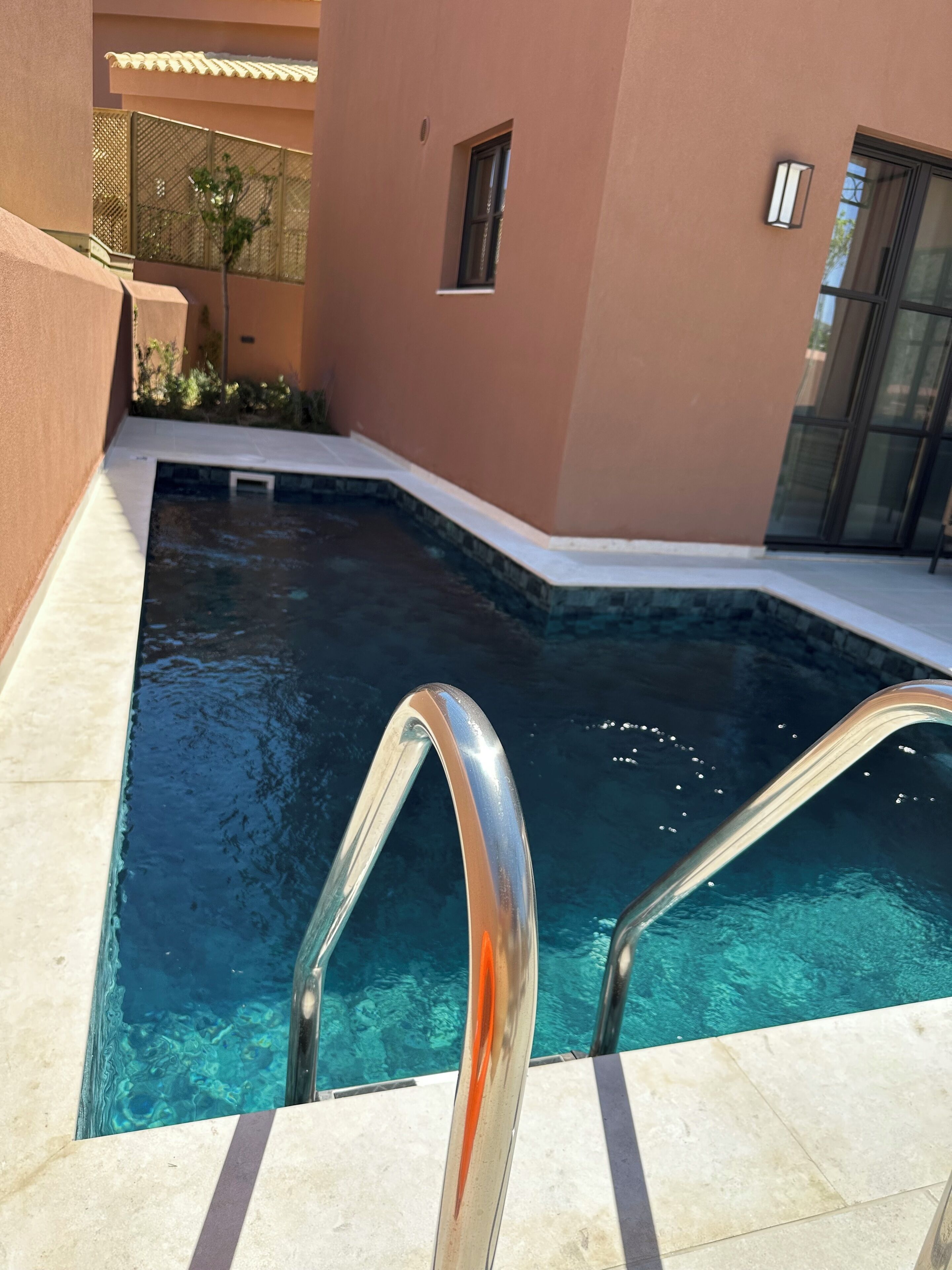 A swimming pool with clear blue water, surrounded by a beige building with a small window and a door.