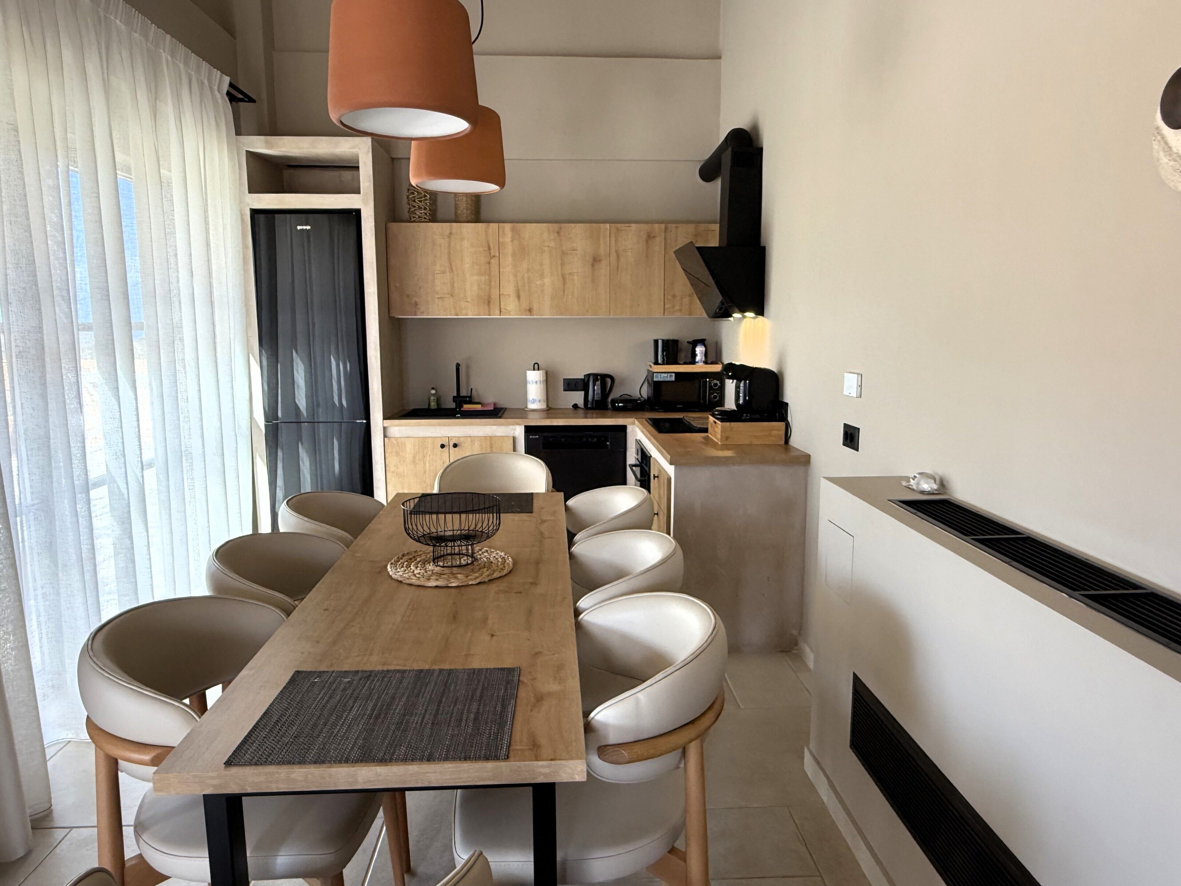 A modern kitchen with wooden cabinets, a dining table with six chairs, and pendant lighting.