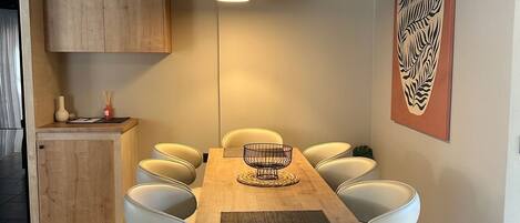 A dining area with a wooden table, white chairs, a woven placemat, and a hanging pendant light.