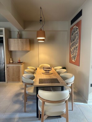 A dining area with a wooden table, white chairs, a woven placemat, and a hanging pendant light. - ARCĀSA Villas Collection by Omilos Hotels (Archanes-Asterousia)