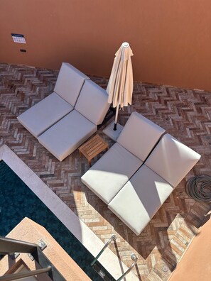 A poolside area with two white lounge chairs, a wooden table, and a beige umbrella. - ARCĀSA Villas Collection by Omilos Hotels (Archanes-Asterousia)