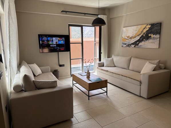 Una sala de estar con dos sofás, una mesa de centro, un televisor montado en la pared y un cuadro colgado.