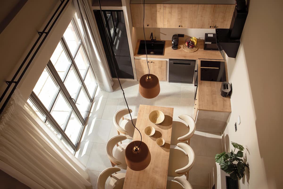 A modern kitchen with a dining area, large windows, and a hanging light fixture.