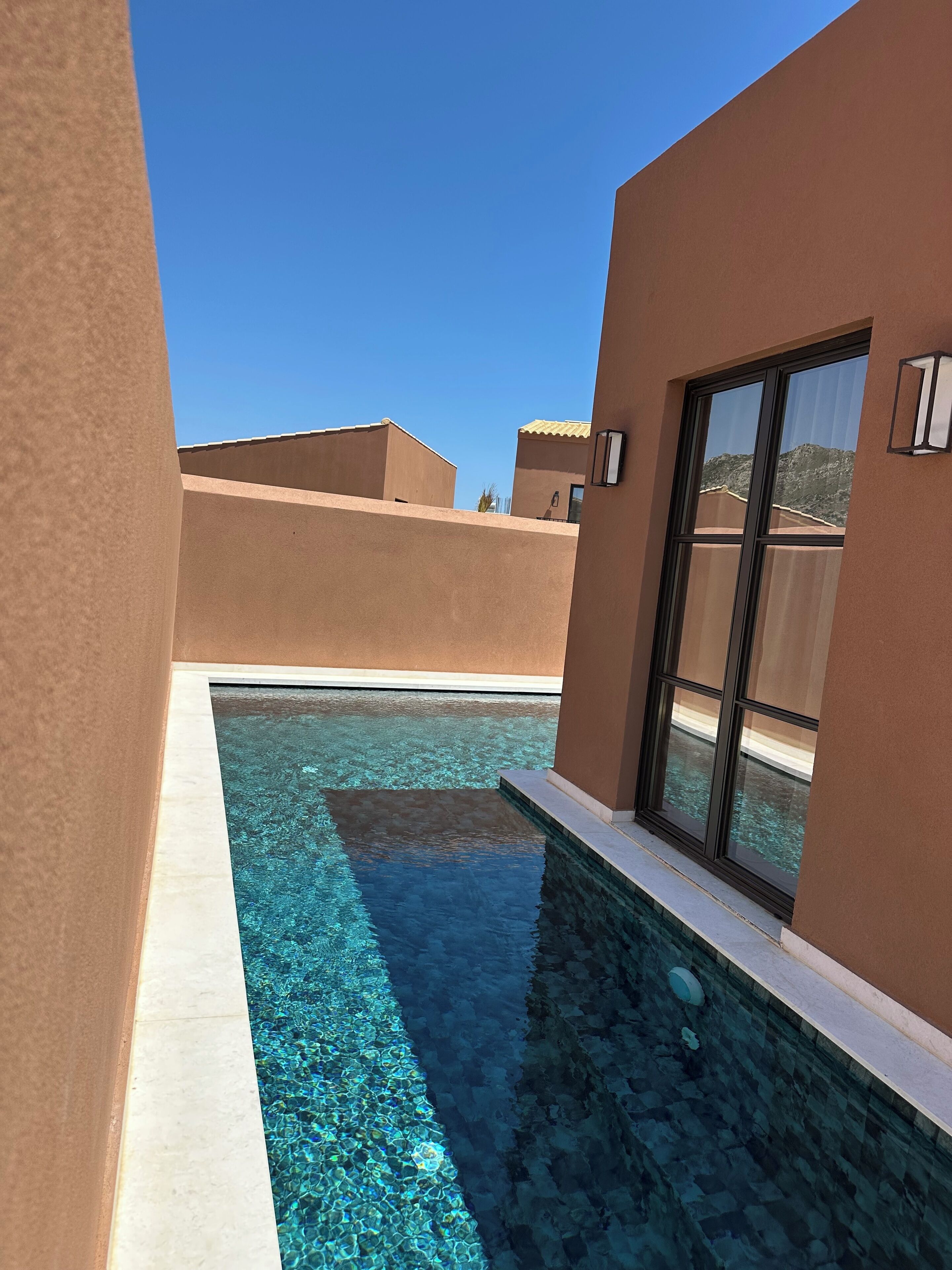 A modern pool area with clear water, surrounded by beige walls and a large window.