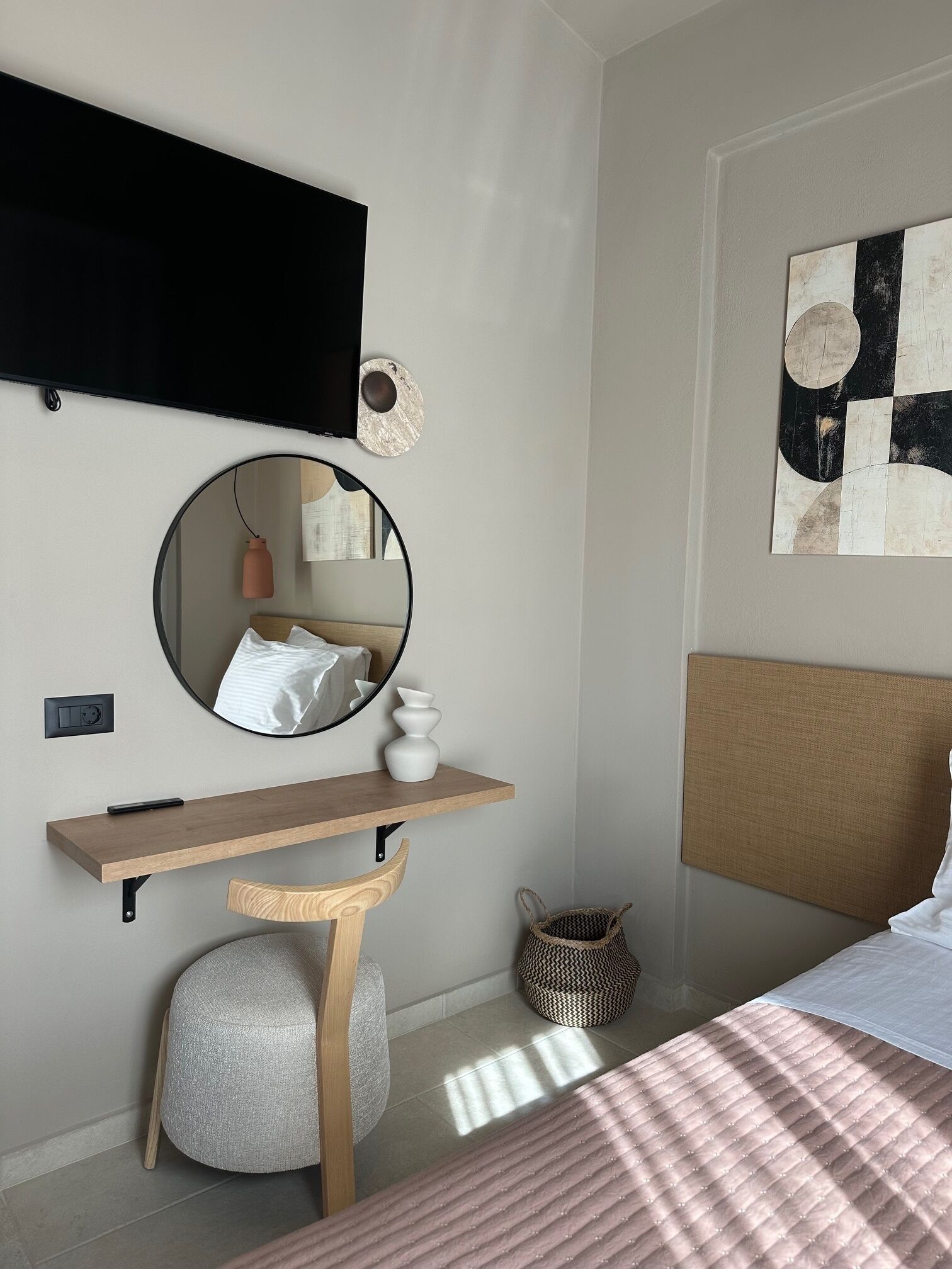 Un dormitorio moderno con cama, mesita de noche, espejo redondo y una obra de arte colgada en la pared.