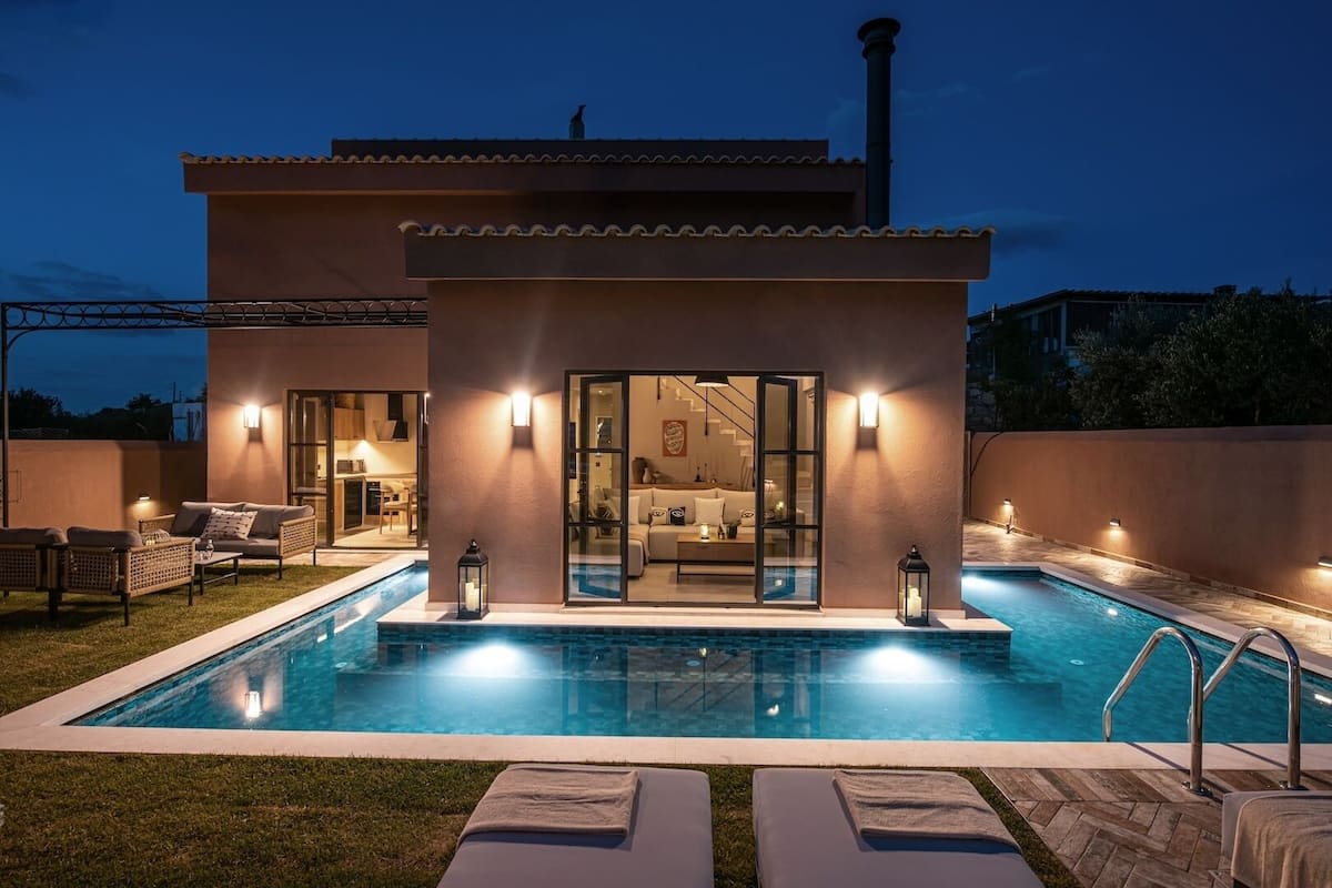 A modern house with a swimming pool, outdoor seating, and a glass door leading to a living area.