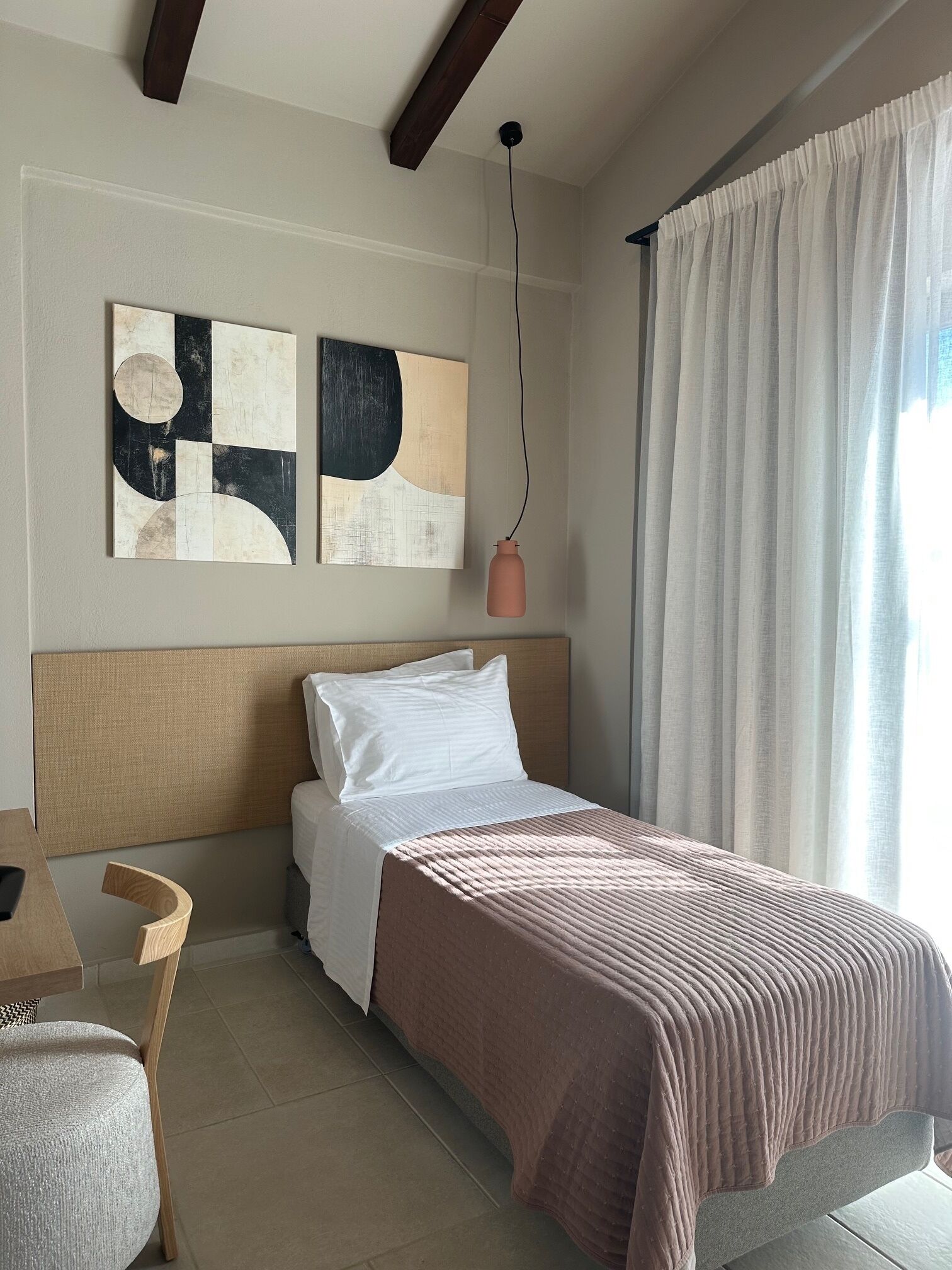 A modern hotel room with a bed, a chair, abstract wall art, and a hanging pendant light.