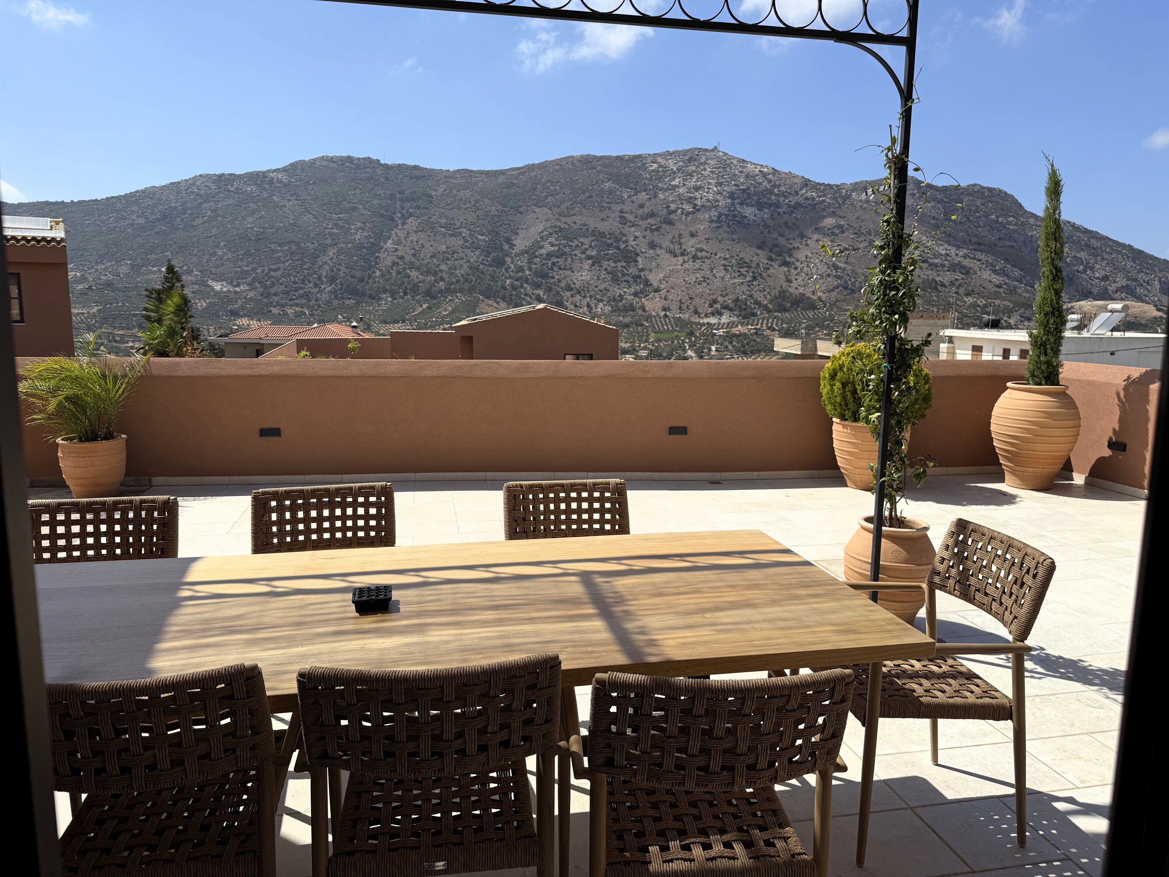 Une terrasse avec une table et des chaises, des plantes en pot et une vue sur une montagne.