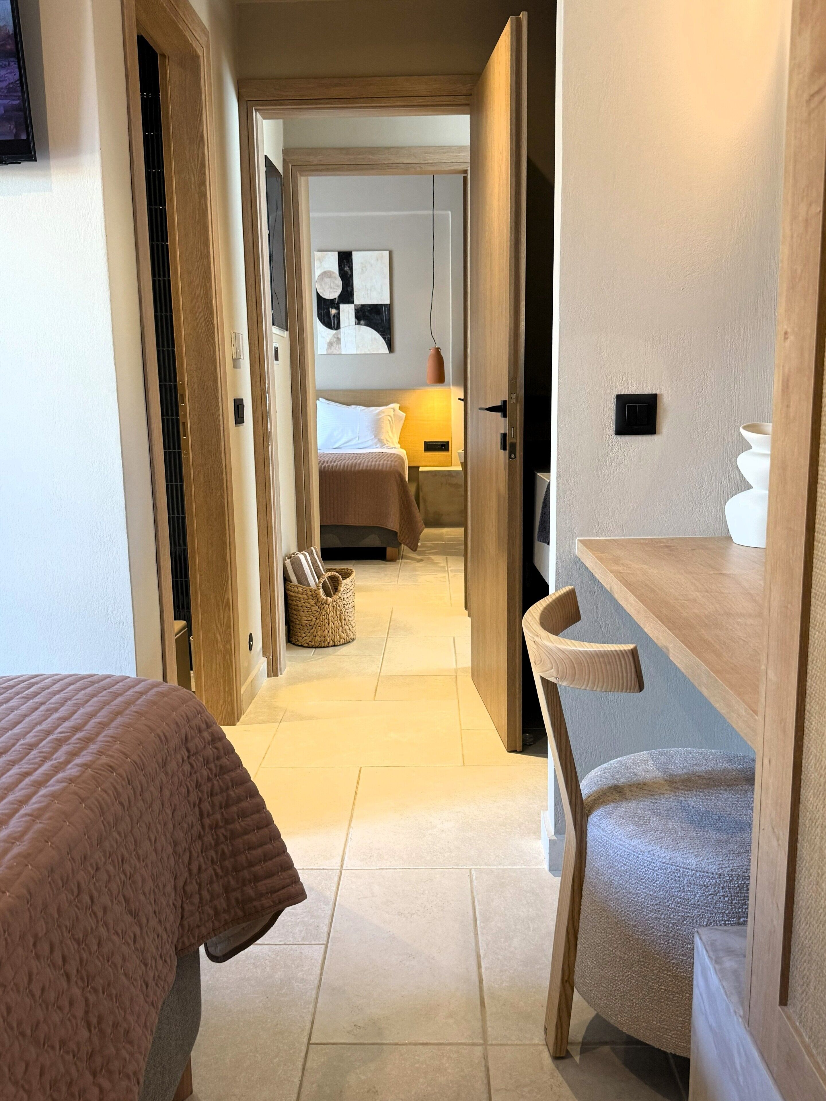 A hotel room with a bed, a chair, a bedside table, a lamp, and a wall-mounted light switch.
