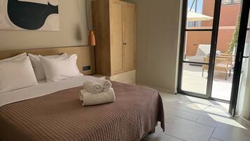 Ett hotellrum med en stor säng, en garderob i trä och utsikt över uteserveringen genom en glasdörr.