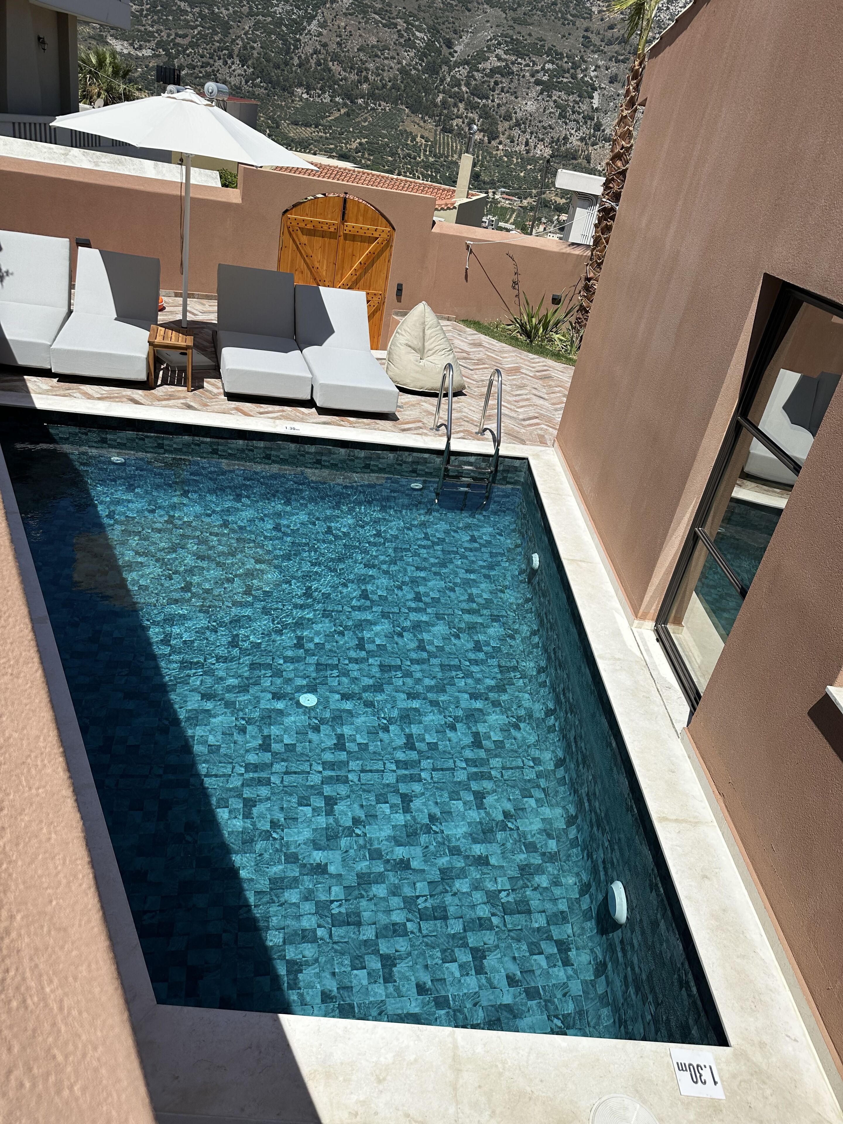 A swimming pool with clear blue water, surrounded by white lounge chairs and a wooden deck.