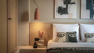 A neatly arranged bedroom with a bed, bedside tables, a vase with dried flowers, abstract art on the wall, and a pendant light.
