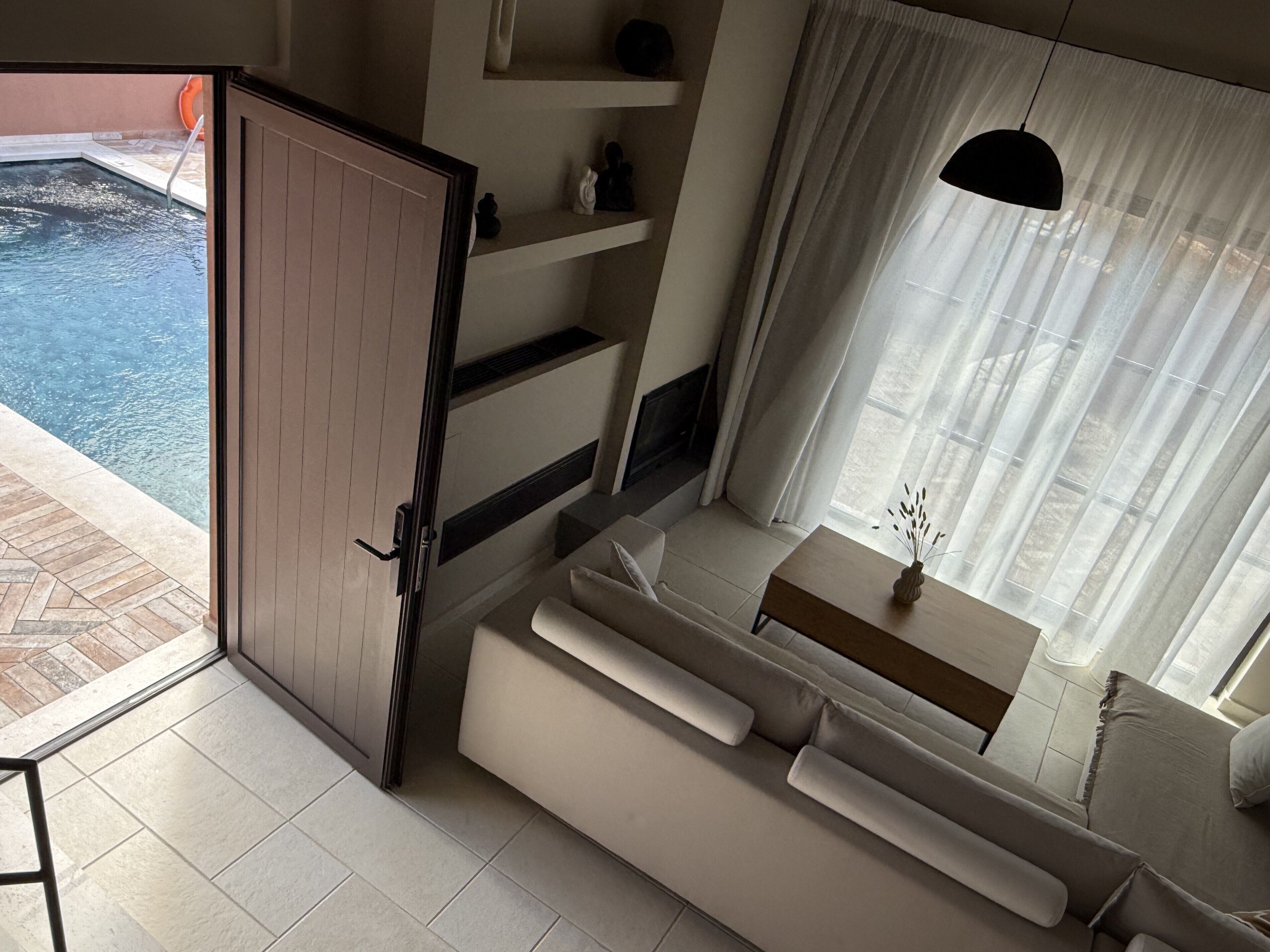 Ein modernes Wohnzimmer mit einer Couch, einem kleinen Tisch und einem Fenster mit transparenten Vorhängen.