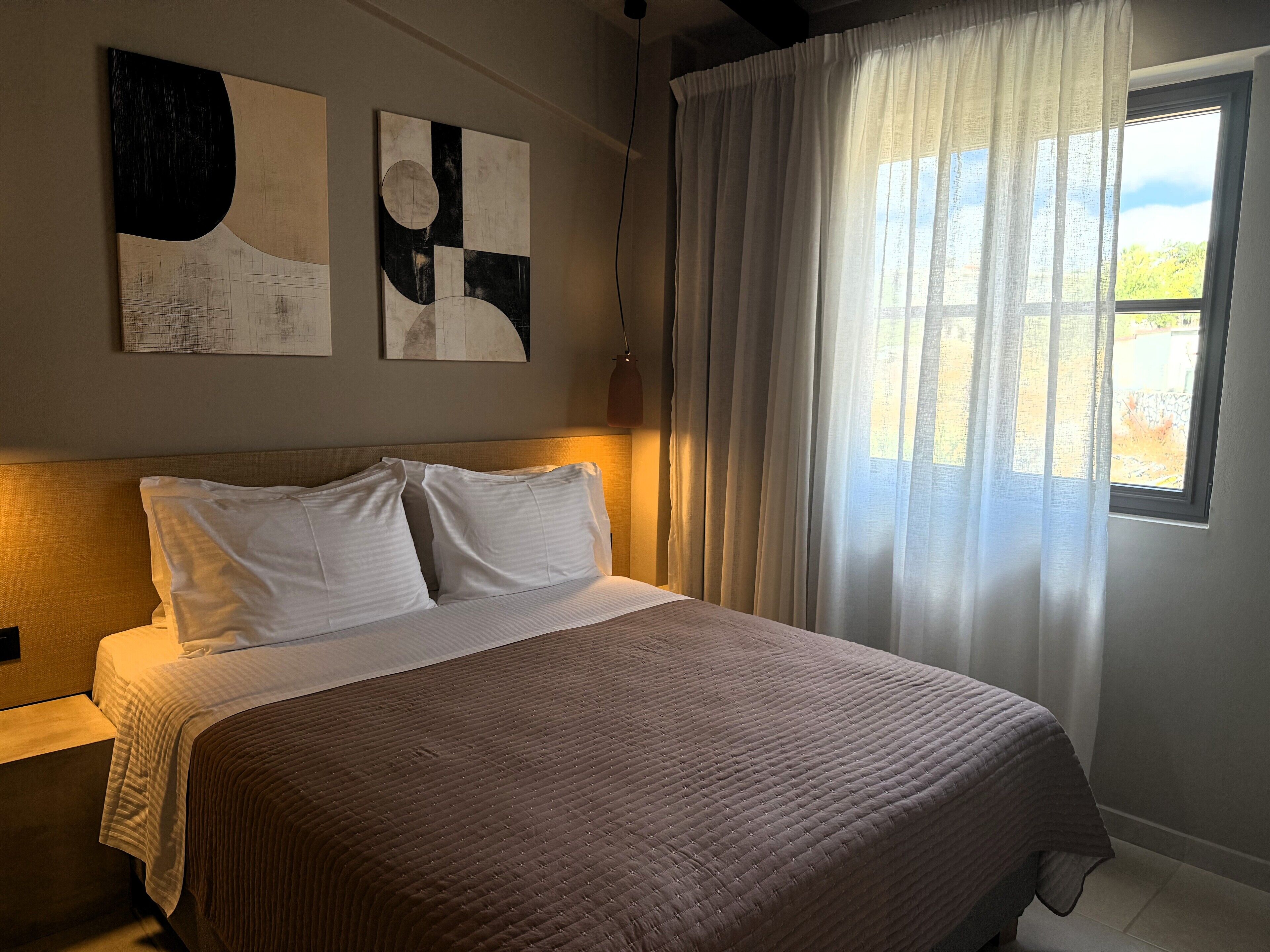 Un dormitorio con una cama grande, ropa de cama blanca y arte abstracto en la pared.