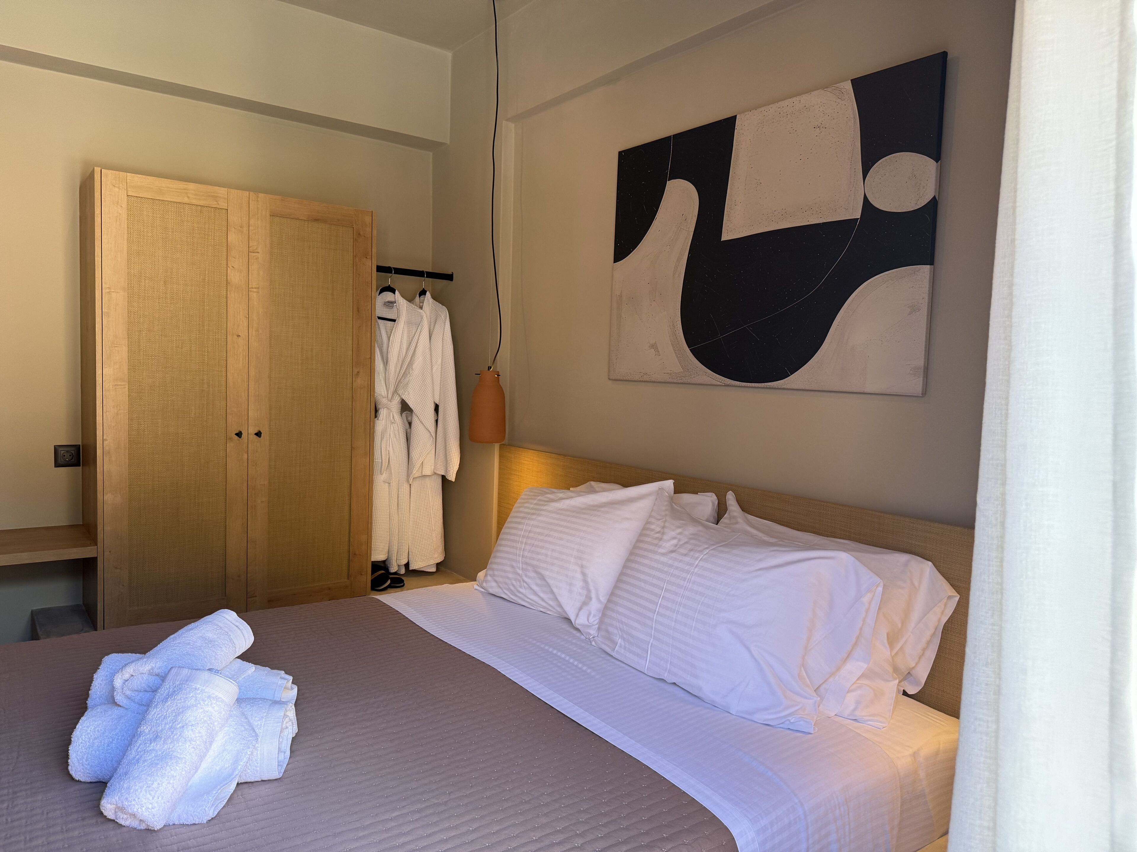 A hotel room with a bed, white towels, a wooden wardrobe, and a wall art piece.