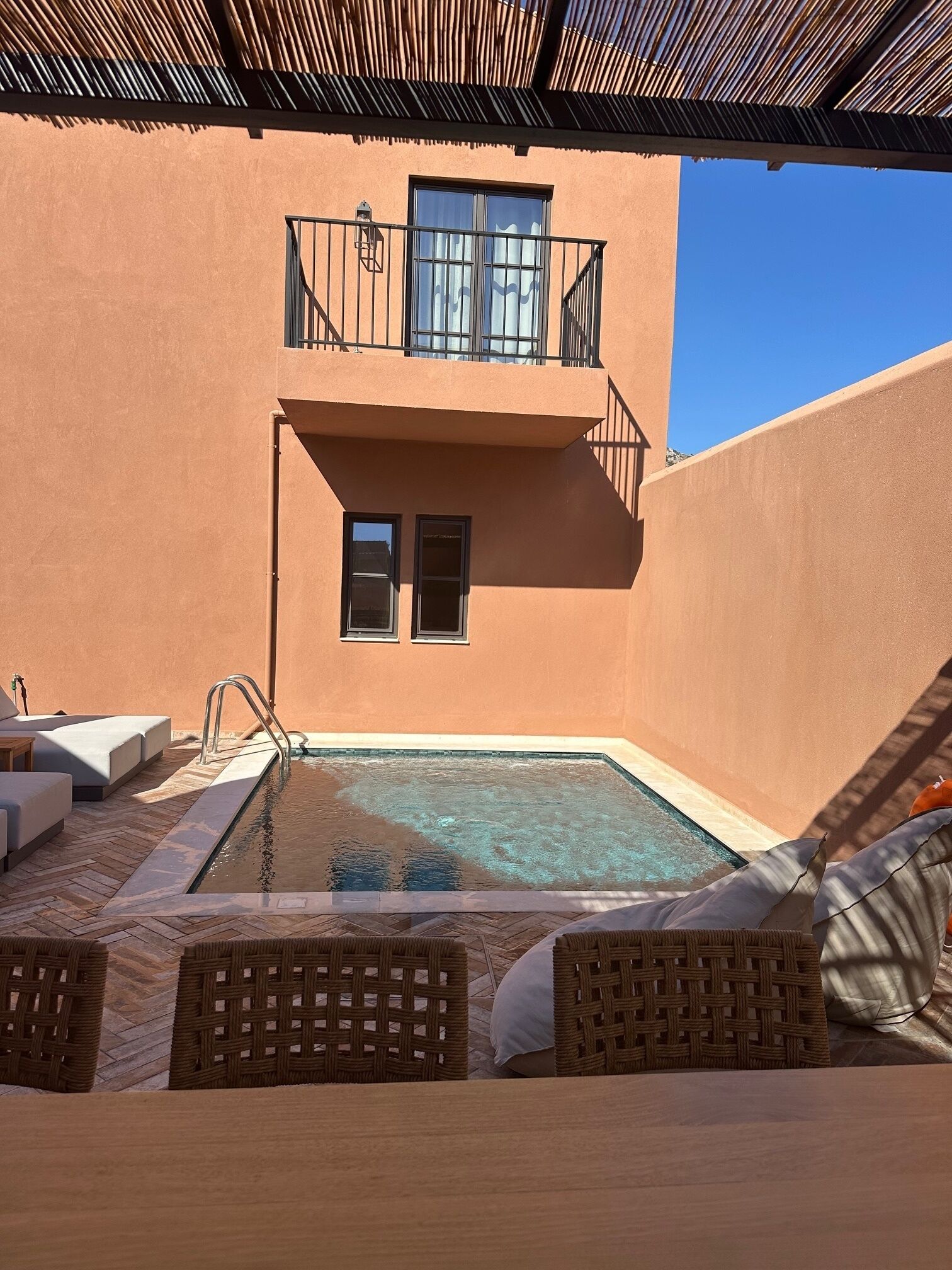 A pool area with a clear view of the pool, lounge chairs, and a building with a balcony.