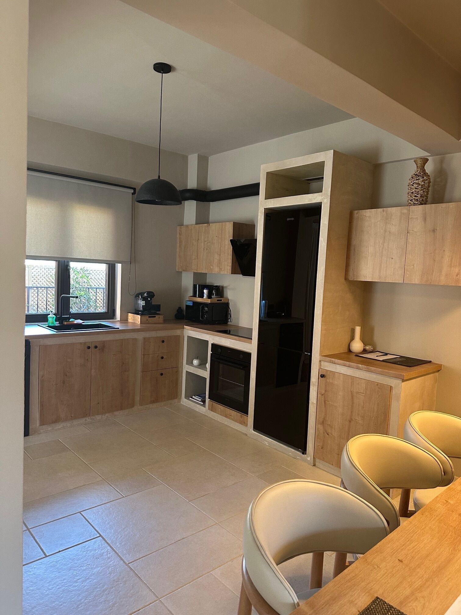 Een moderne keuken met houten kastjes, een inbouwoven en een zithoek met twee stoelen.