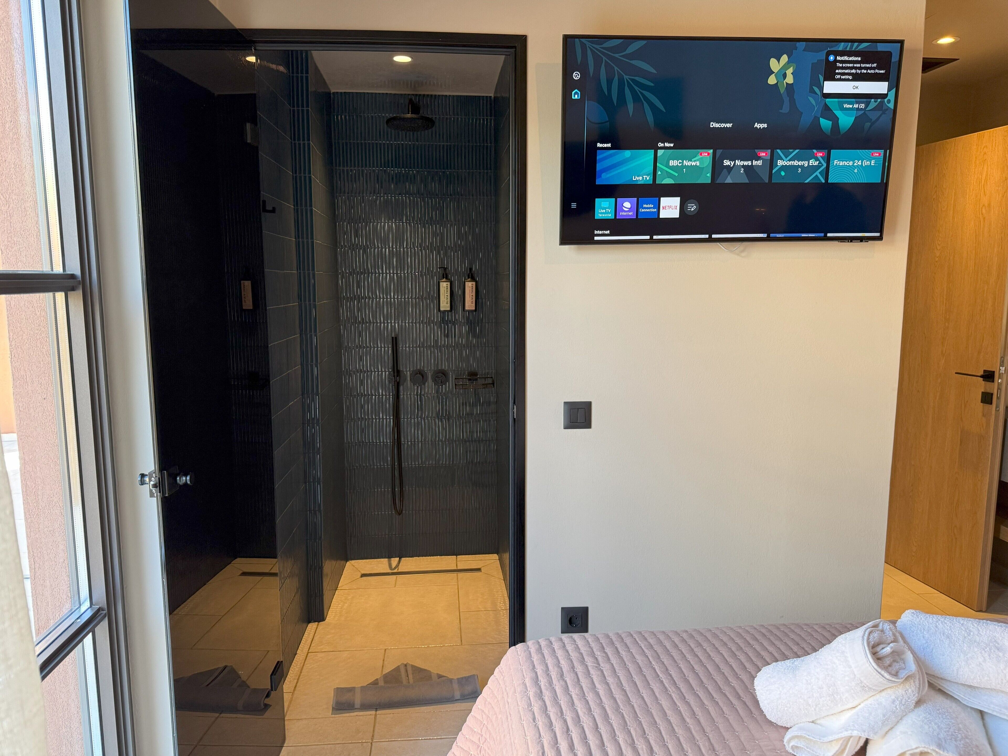 A hotel room with a large flat-screen TV mounted on the wall displaying various channels and apps.