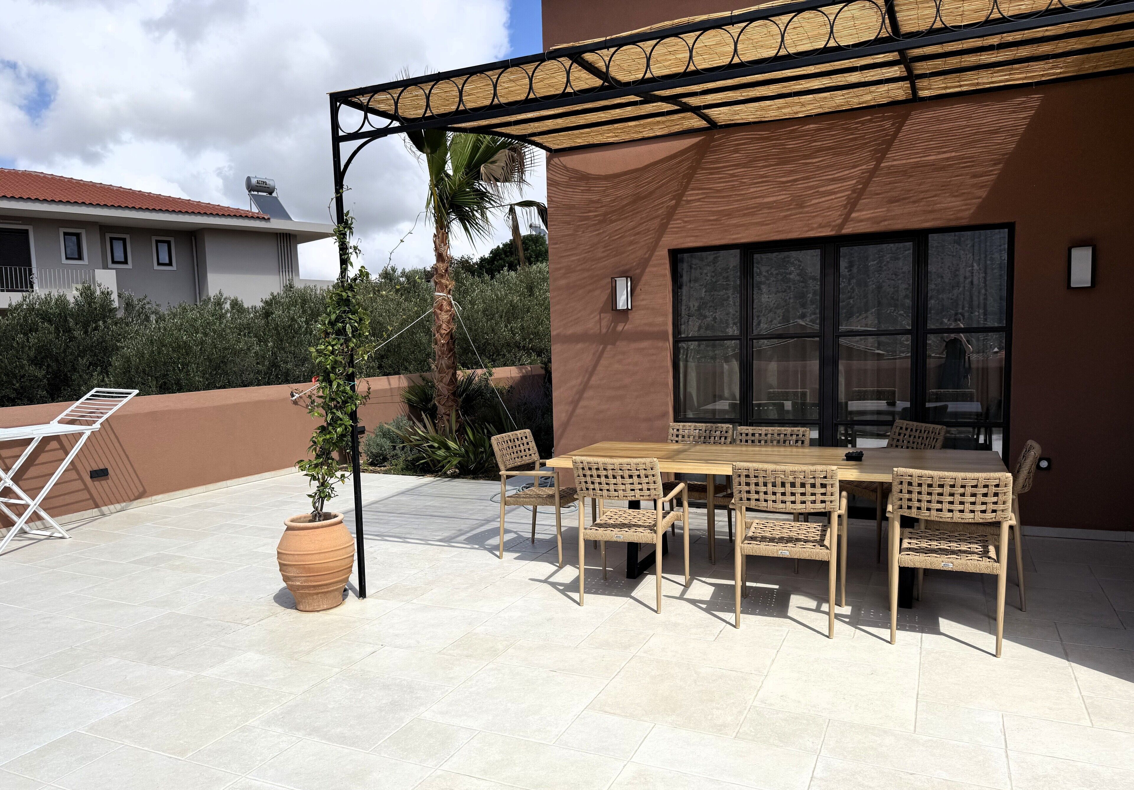 Eine Außenpatio mit Tisch und Stühlen, einer großen Kübelpflanze und einer Pergola, die Schatten spendet.
