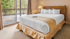 A hotel room with a large bed, a wooden headboard, a nightstand with a lamp, and a view of the outdoors through a sliding glass door. - 3 Bedroom Condo at Key Condo in Keystone (Keystone)