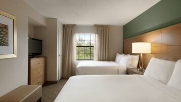 A hotel room with two beds, a television, a desk, and a window with curtains.