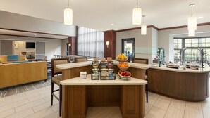 Una hall moderna di un hotel con un'area bar centrale, diverse disposizioni di posti a sedere e un'ampia finestra che offre luce naturale.