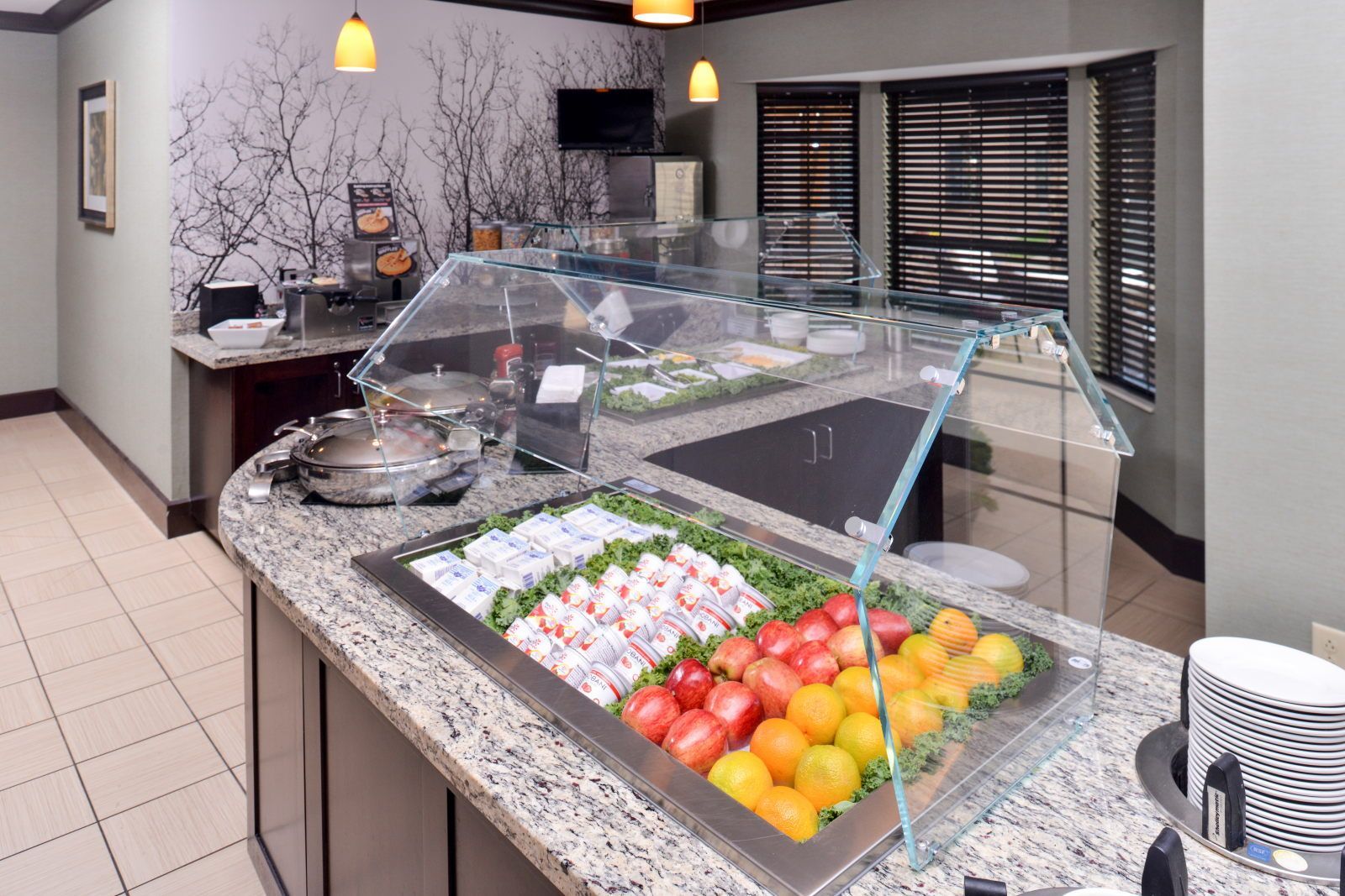 A buffet area with a variety of food items, including fruits and dairy products, in a modern setting with a glass display case.