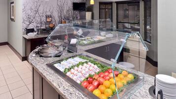 A buffet area with a variety of food items, including fruits and dairy products, in a modern setting with a glass display case.