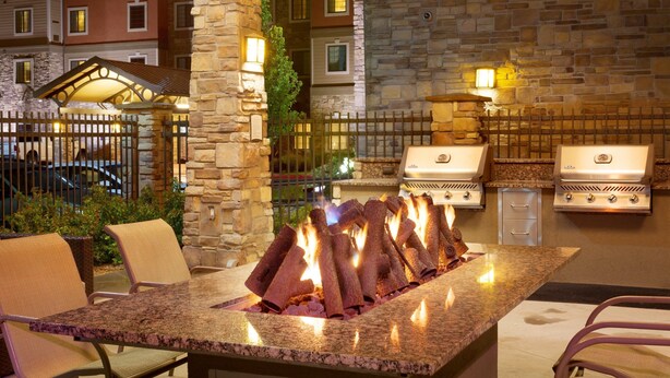 An outdoor kitchen with a stone wall, two gas grills, and a fire pit.