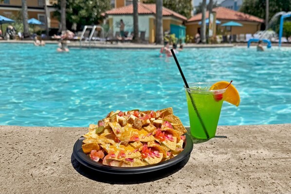 A poolside view with a plate of nachos and a green drink with an orange slice garnish.