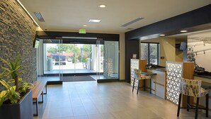 A modern lobby with a glass door entrance, a reception desk, and a seating area with a bench and chairs. - Free Breakfast. Gym. Near Medical Center. (Little Rock)