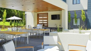 An outdoor patio area with a wooden ceiling, white chairs, a table, and a grill. - Free Breakfast. Gym. Near Medical Center. (Little Rock)
