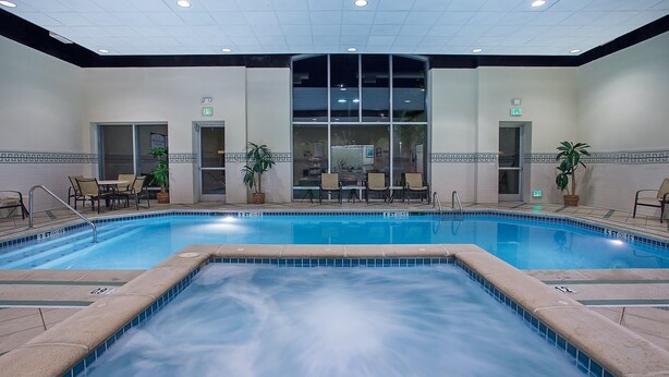 Une grande piscine intérieure à l’eau claire, entourée de chaises longues et de tables, avec vue sur le hall d’entrée.