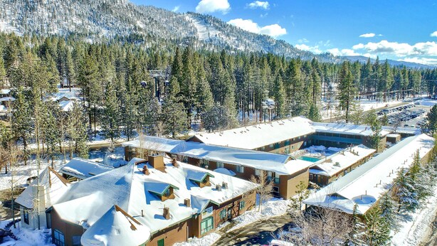A snow-covered residential area with multiple houses, a parking lot, and a mountainous backdrop.