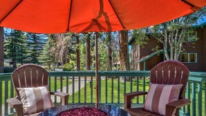 A wooden deck with two Adirondack chairs and a round table with a fire pit.