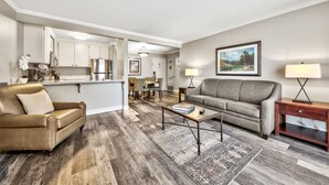A living room with a sofa, coffee table, and a dining area in the background.