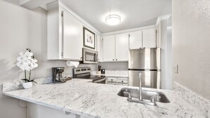 A modern kitchen with white cabinetry, a stainless steel refrigerator, a built-in oven, and a marble countertop.
