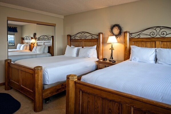 Habitación de hotel con dos camas de madera, una mesita de noche con lámpara y un espejo que refleja la habitación.